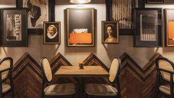 A dining area with a wooden table and chairs, surrounded by framed artwork on the walls.