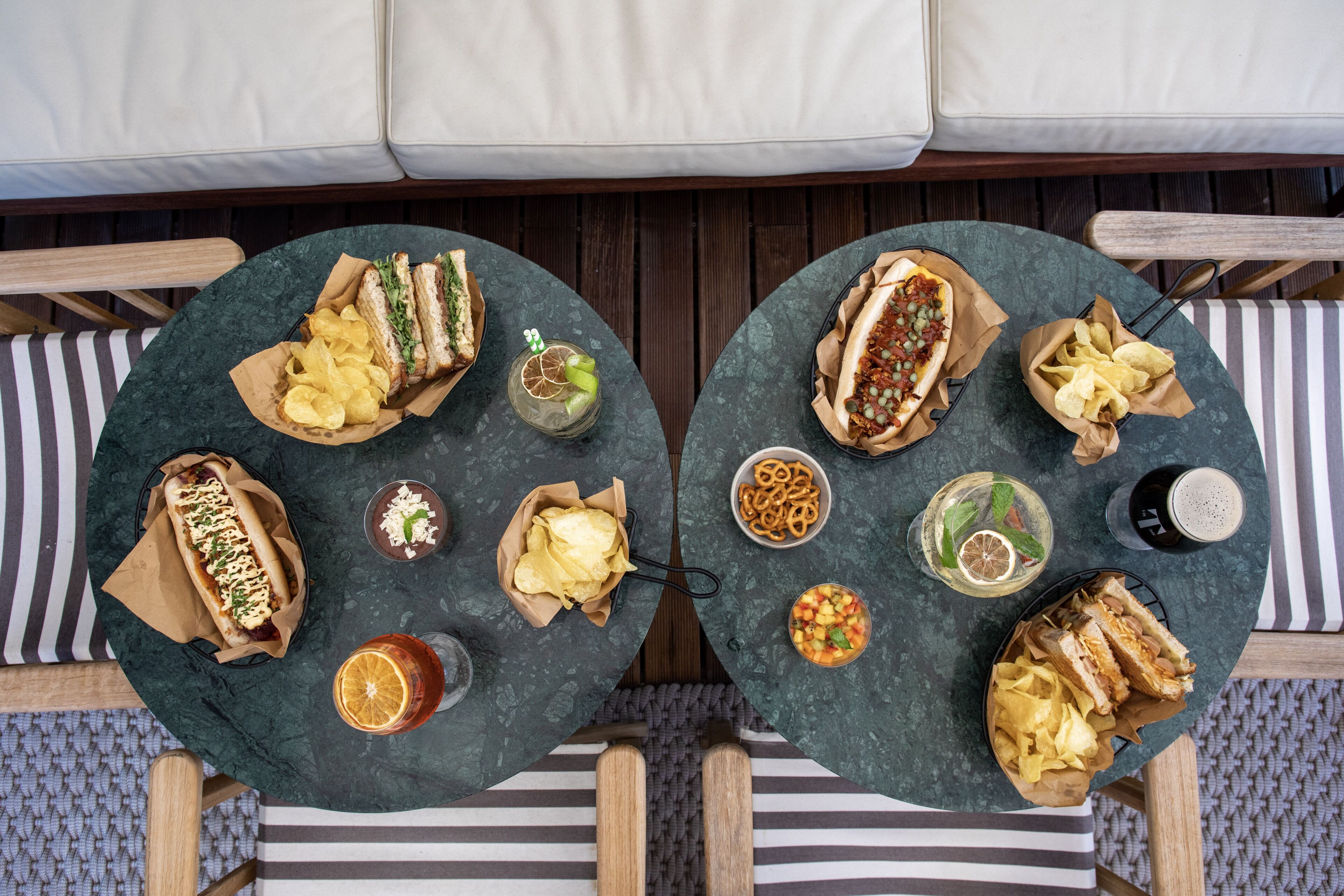 Two round tables with food and drinks, surrounded by striped cushions and wooden chairs.