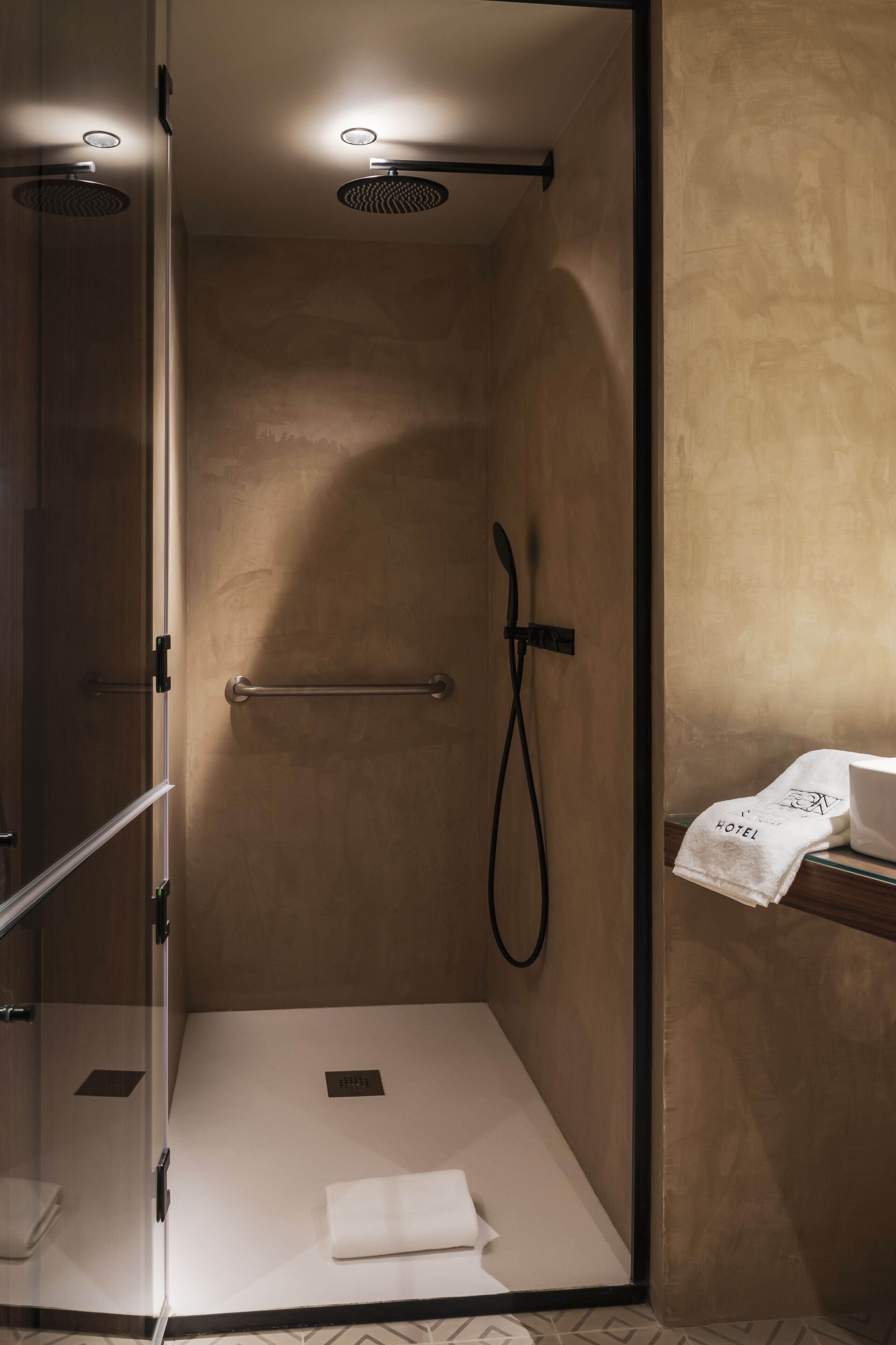 Un espace douche moderne doté d’une porte en verre, d’un porte-serviettes et d’une petite étagère sur laquelle est posée une serviette.
