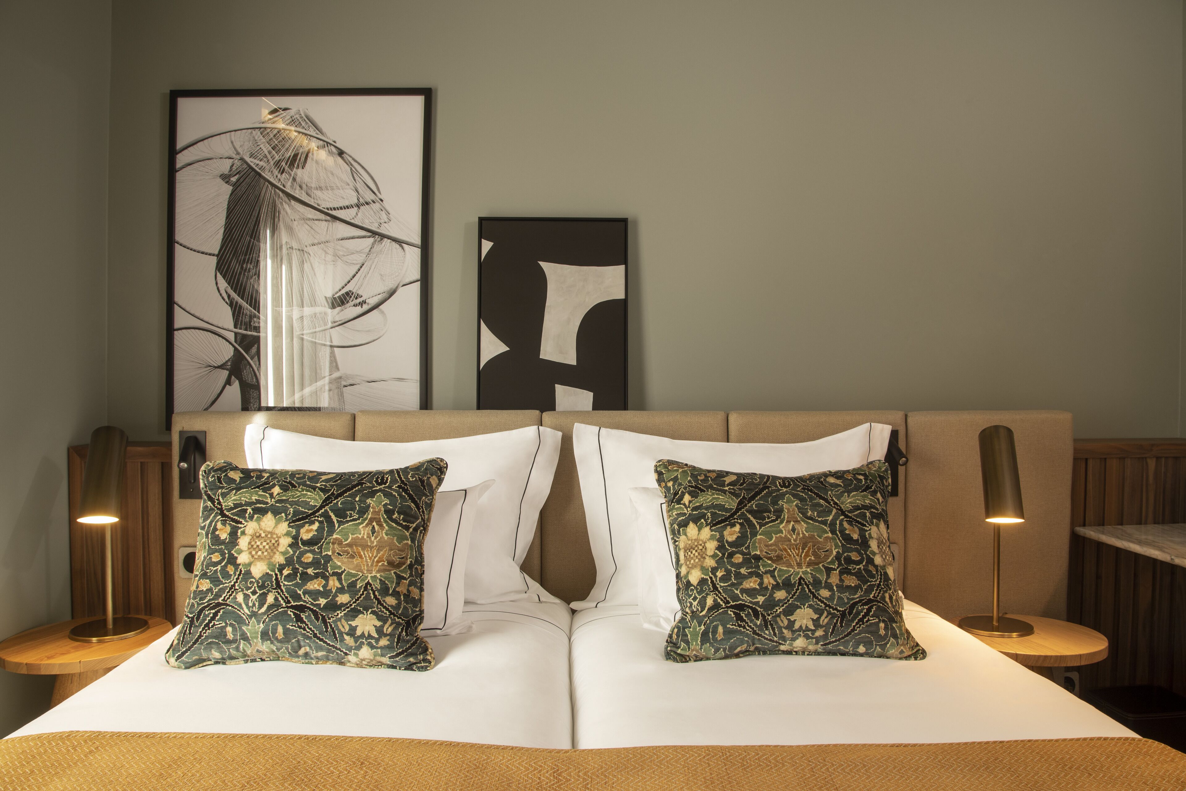 A neatly made bed with two decorative pillows, a framed abstract artwork above, and a lamp on a bedside table.