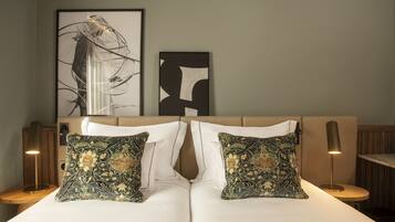 A neatly made bed with two decorative pillows, a framed abstract artwork above, and a lamp on a bedside table.