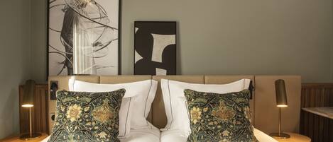 A neatly made bed with two decorative pillows, a framed abstract artwork above, and a lamp on a bedside table.