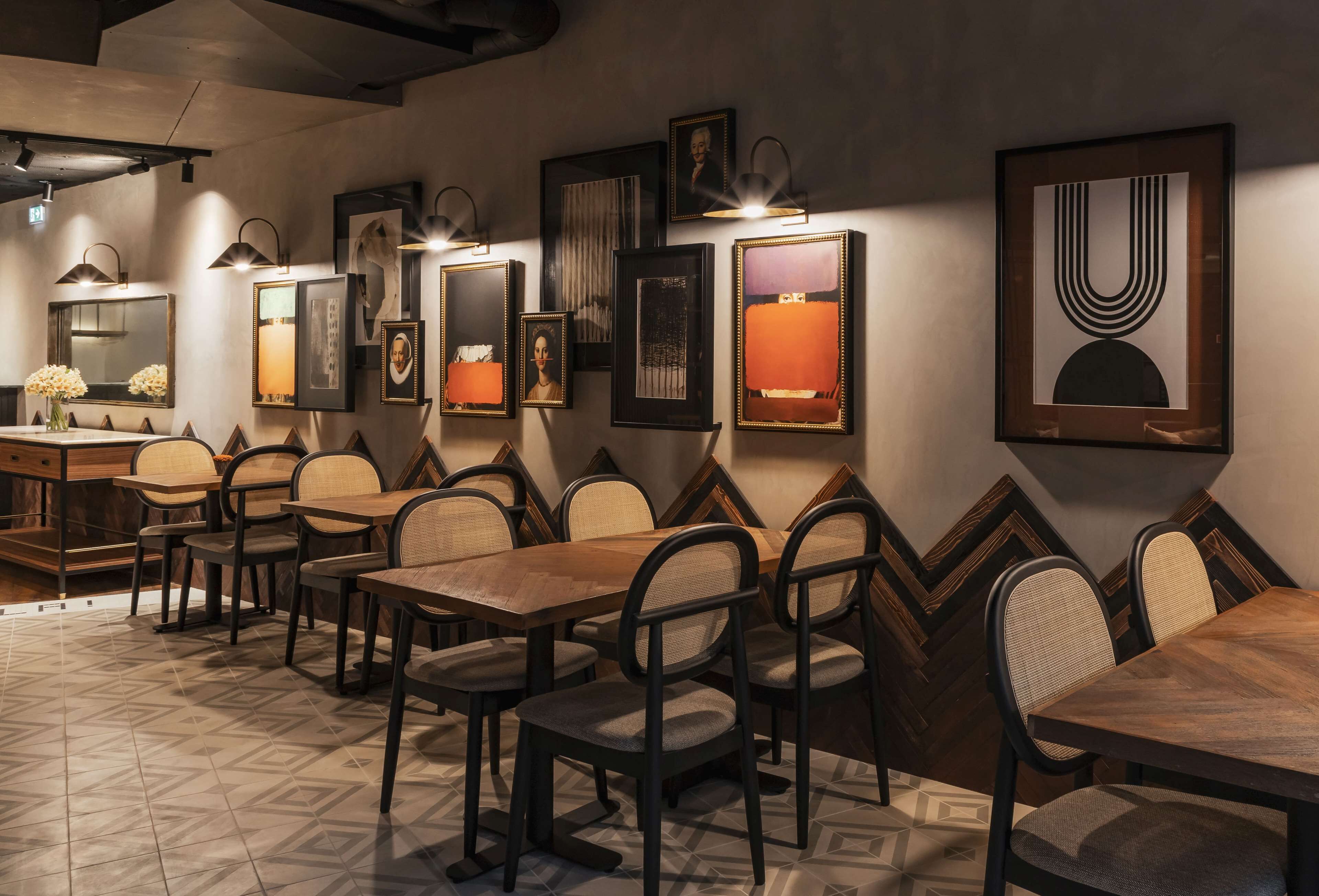 A restaurant with a long wooden table and chairs, framed artwork on the walls, and a patterned floor.