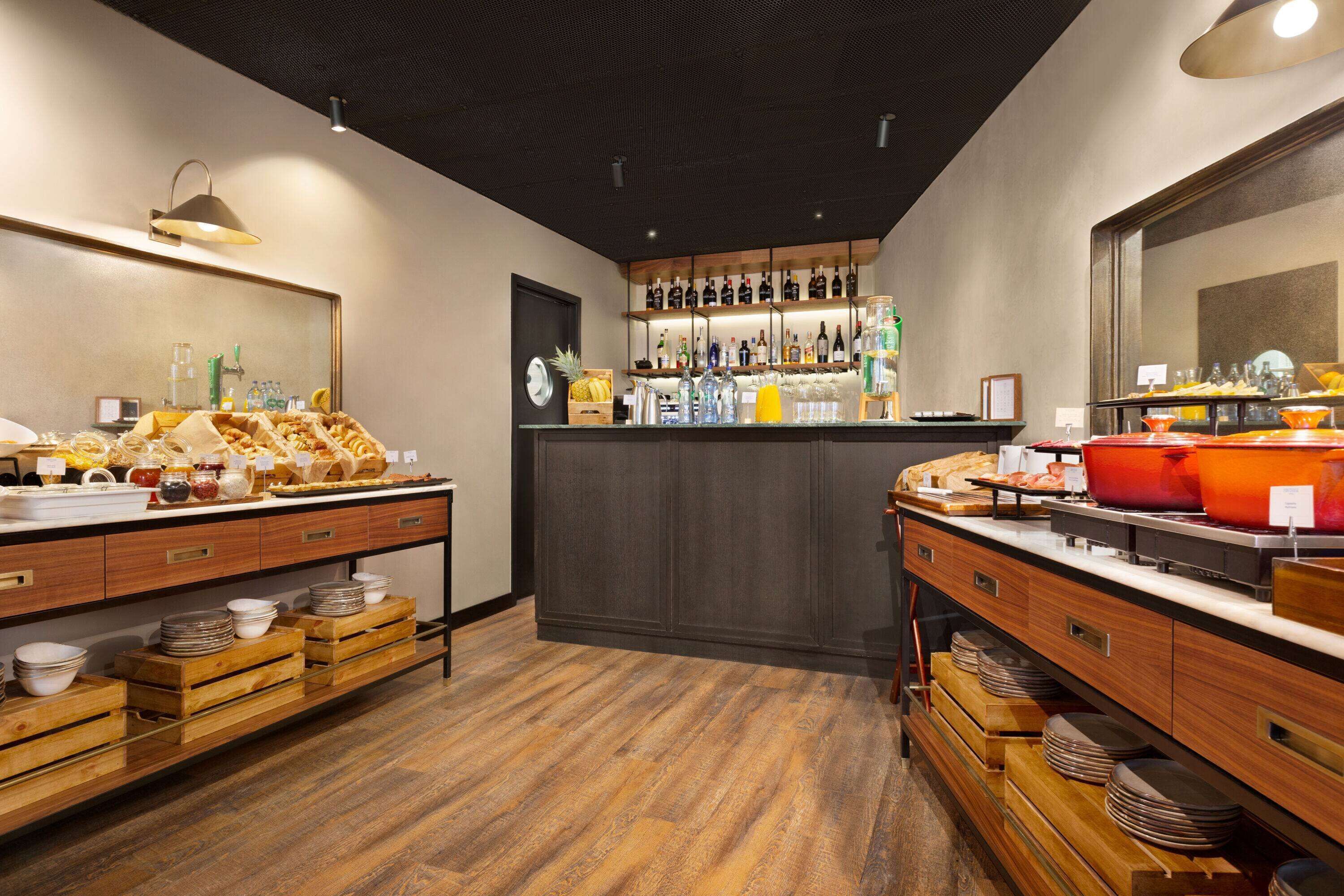 A breakfast buffet with wooden counters, a variety of food items, and a bar area with bottles and glasses.