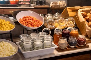 Buffet com diversos alimentos, incluindo batatas em cubos, cenouras e vários potes de acompanhamentos.