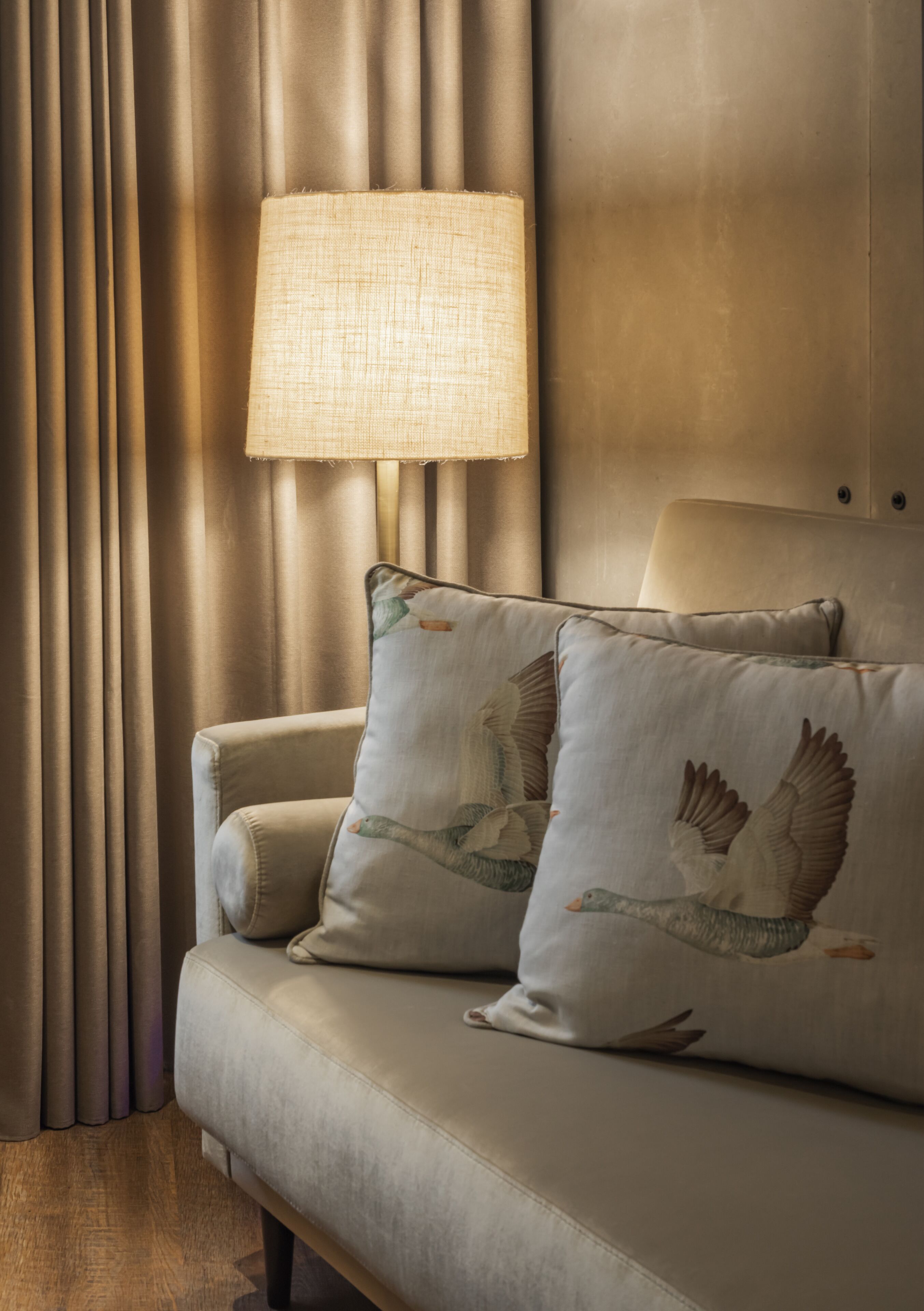 A sofa with two pillows featuring bird designs, a lamp, and curtains.