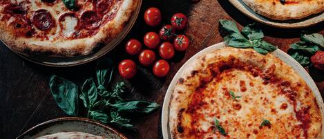 Three pizzas with various toppings and fresh tomatoes on a wooden table.