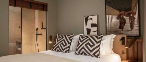 Una habitación de hotel moderna con una cama grande, un armario de madera, una mesita de noche con una lámpara y un cuadro enmarcado en la pared.