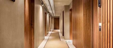 Un pasillo de hotel con paneles de madera, suelo de baldosas y flechas indicativas, e iluminación en el techo.