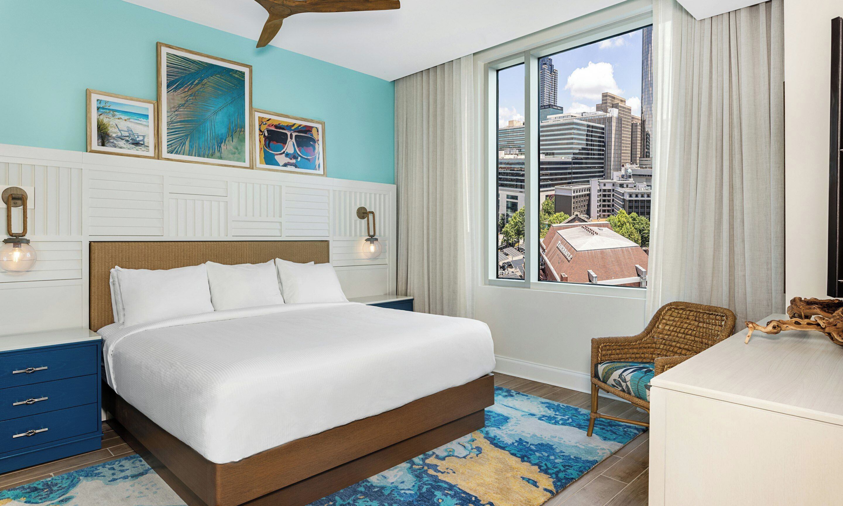 A hotel room with a bed, a chair, a desk, and a large window with a city view.