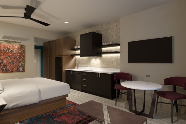 A modern hotel room with a bed, a small kitchenette, a dining area with two chairs, and a large TV on the wall.