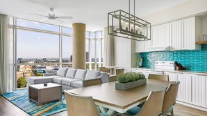 A modern living room with a sofa, coffee table, and dining table, large windows with a city view, and a kitchen with white cabinets and a blue backsplash. - Margaritaville Vacation Club – Atlanta (Atlanta)