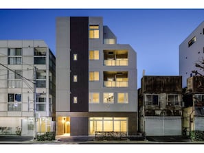 Un edificio de varios pisos con un diseño moderno, que presenta una combinación de balcones y ventanas, y una entrada a nivel de calle con un aparcamiento para bicicletas.