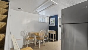 A compact kitchen with a dining area, a refrigerator, and a window with blinds.