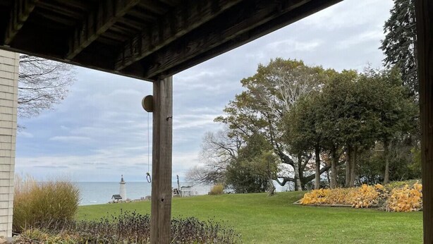A covered outdoor area with a view of a grassy landscape, trees, and a body of water.