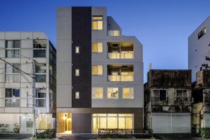 A multi-story building with a modern architectural design, featuring a mix of balconies and windows, and a well-lit entrance.
