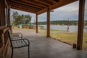 Un espacio al aire libre techado con un banco, vista a un lago y un edificio pequeño al fondo.