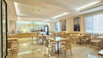 A modern dining area with tables and chairs, a kitchen in the background, and artwork on the walls.