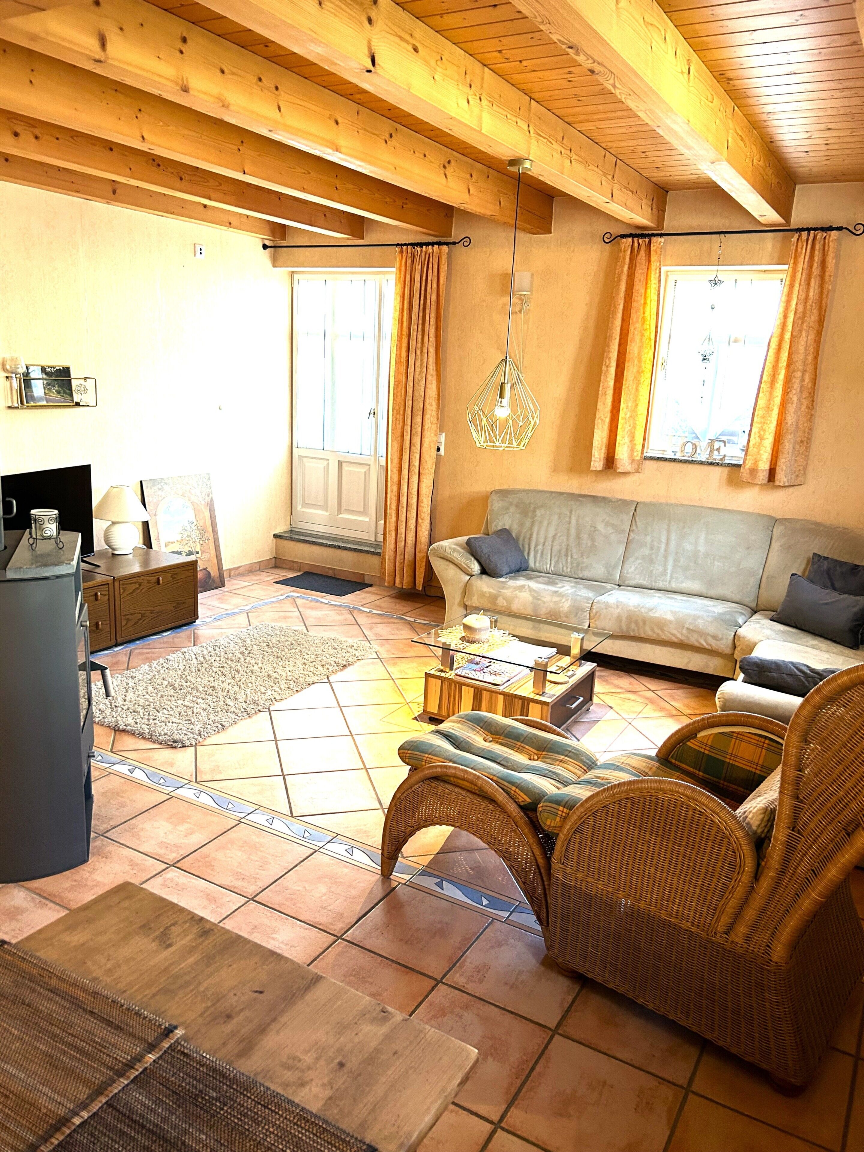 Ein Wohnzimmer mit einer Couch, Korbstühlen, einem Couchtisch und einem Fernseher.