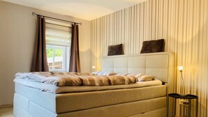 Un dormitorio con una cama grande, una mesita de noche con lámpara y una ventana con cortinas.