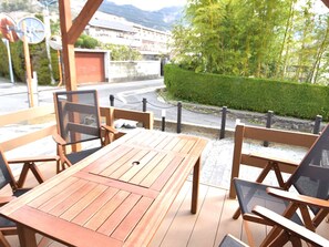 Un conjunto de mesa y sillas de madera al aire libre, con vista a una carretera y vegetación.
