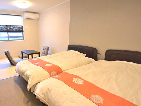 Habitación de hotel con dos camas, una mesita, una silla y una ventana con persianas.