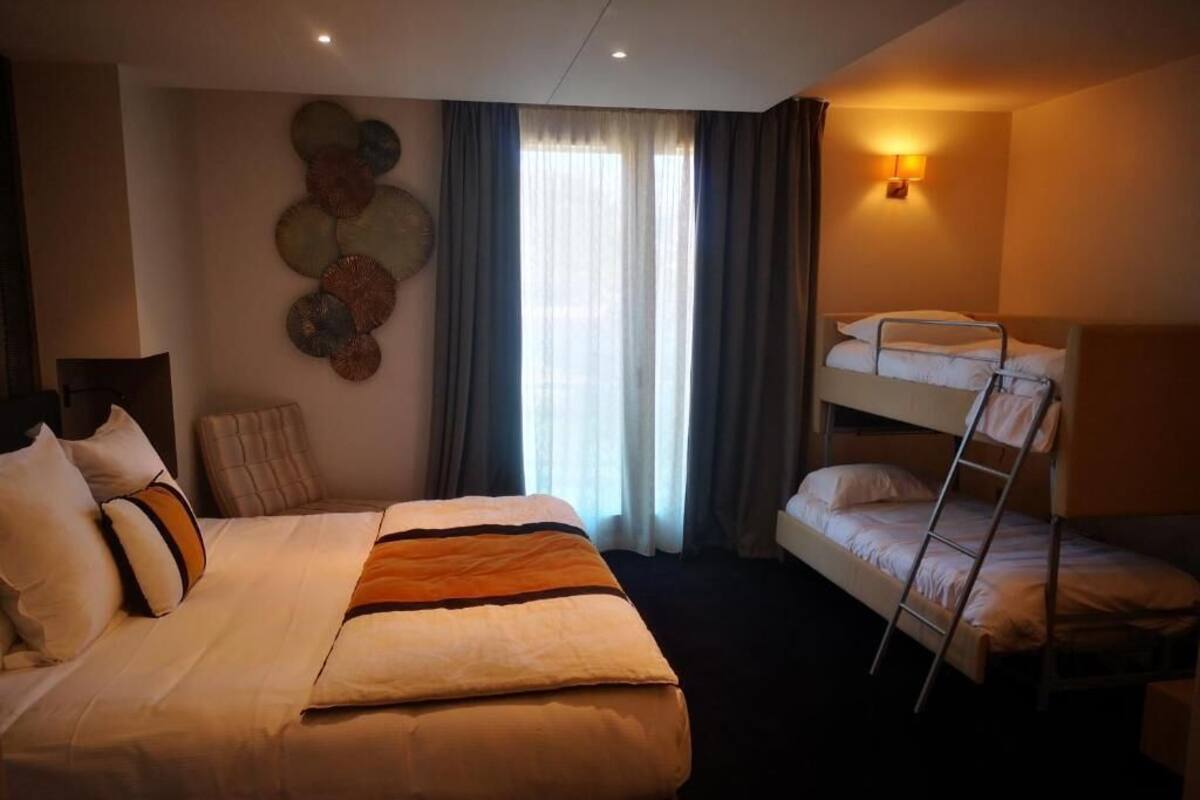 Una habitación de hotel con una cama individual, una cama litera, una lámpara de pared y un adorno mural.