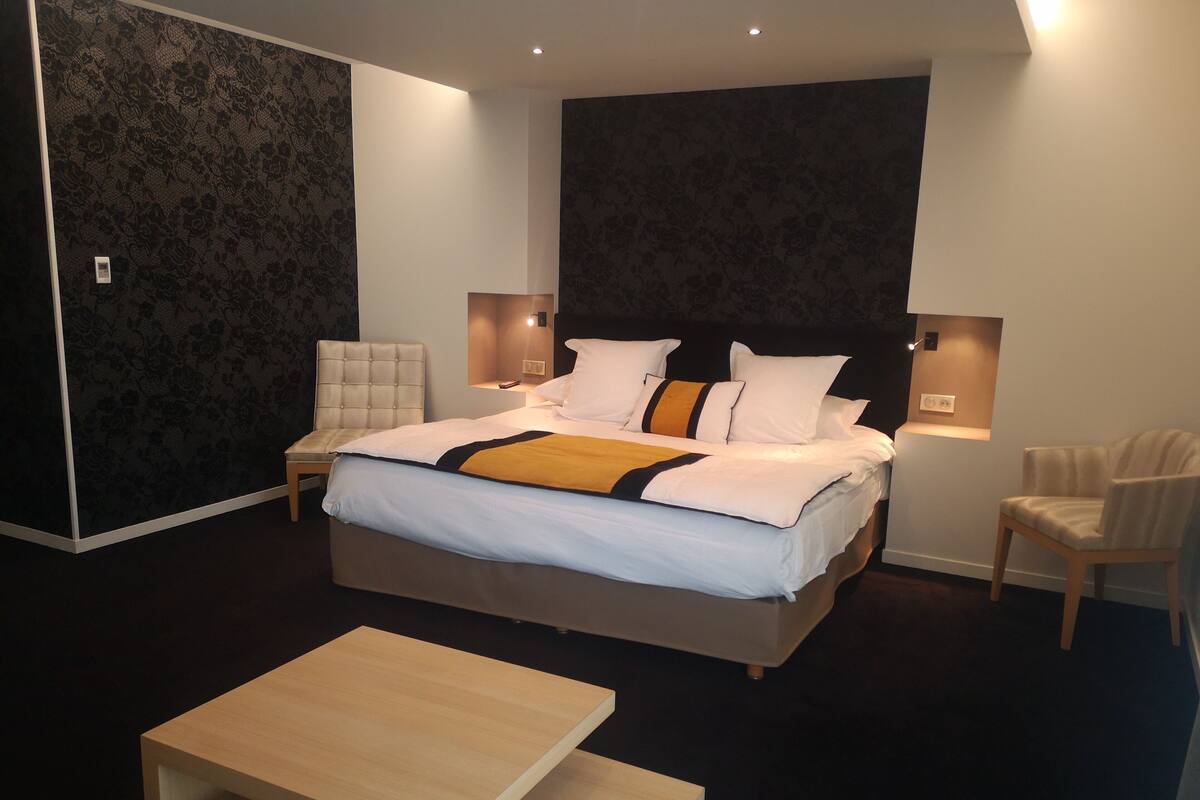 Un dormitorio moderno con una cama grande, dos mesitas de noche, una silla y una pequeña mesa.