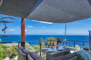 Een balkon met uitzicht op zee, rieten meubilair en een gedekte tafel.