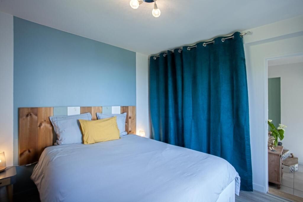 Un dormitorio con cabecera de madera, cama con ropa de cama blanca y amarilla, y cortina azul.