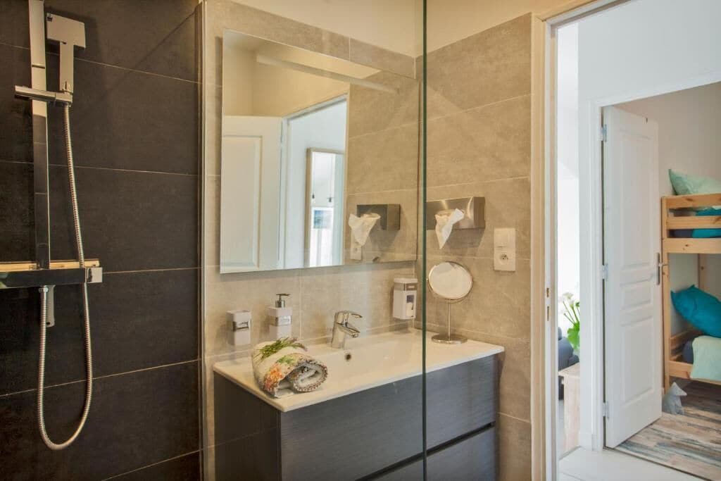 Un baño moderno con cabina de ducha de vidrio, un espejo grande y un tocador con lavabo y toallero.