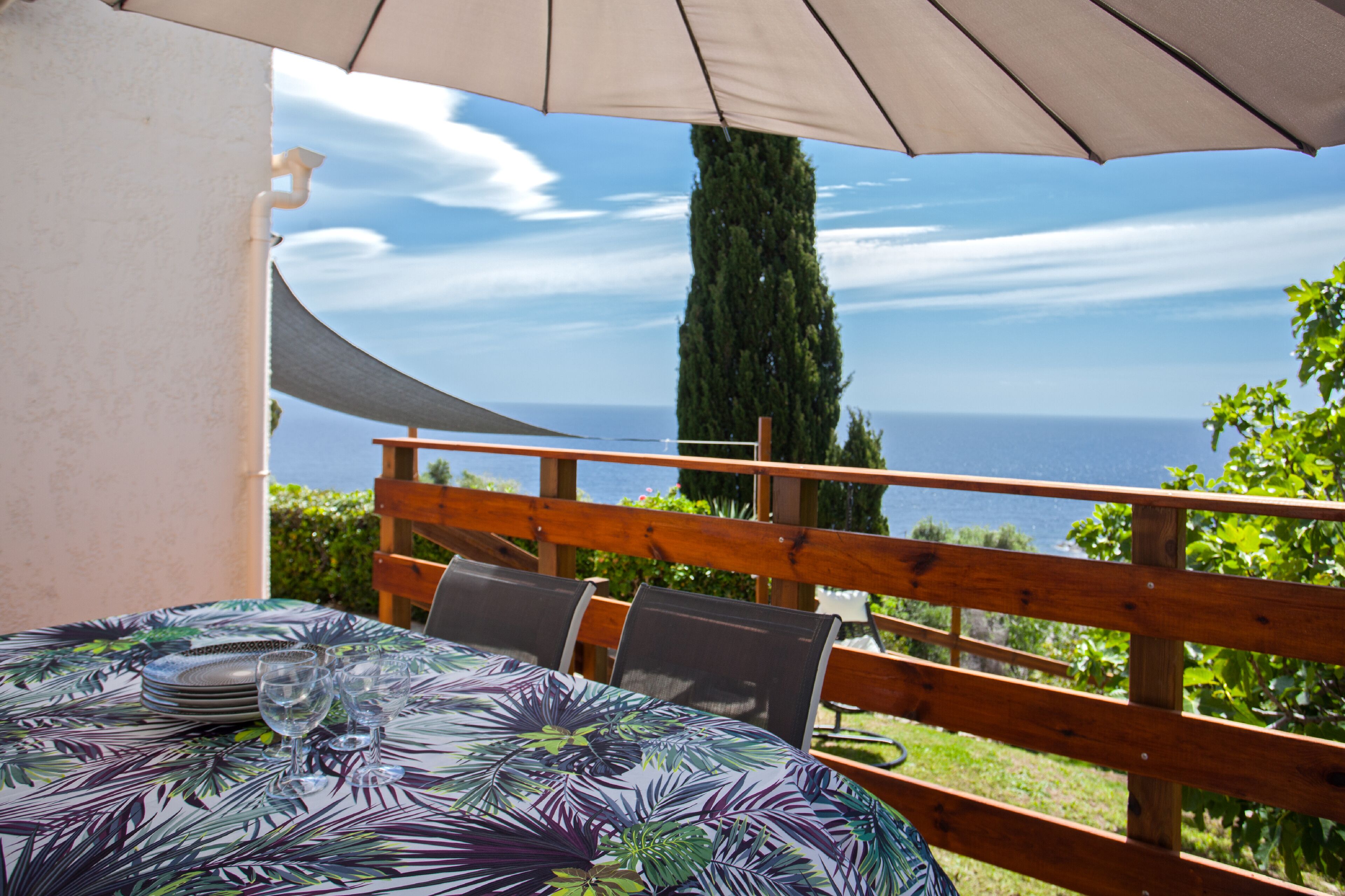 A table with a tropical leaf pattern tablecloth, a wooden fence, and a view of the sea.