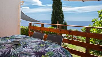 A table with a tropical leaf pattern tablecloth, a wooden fence, and a view of the sea.
