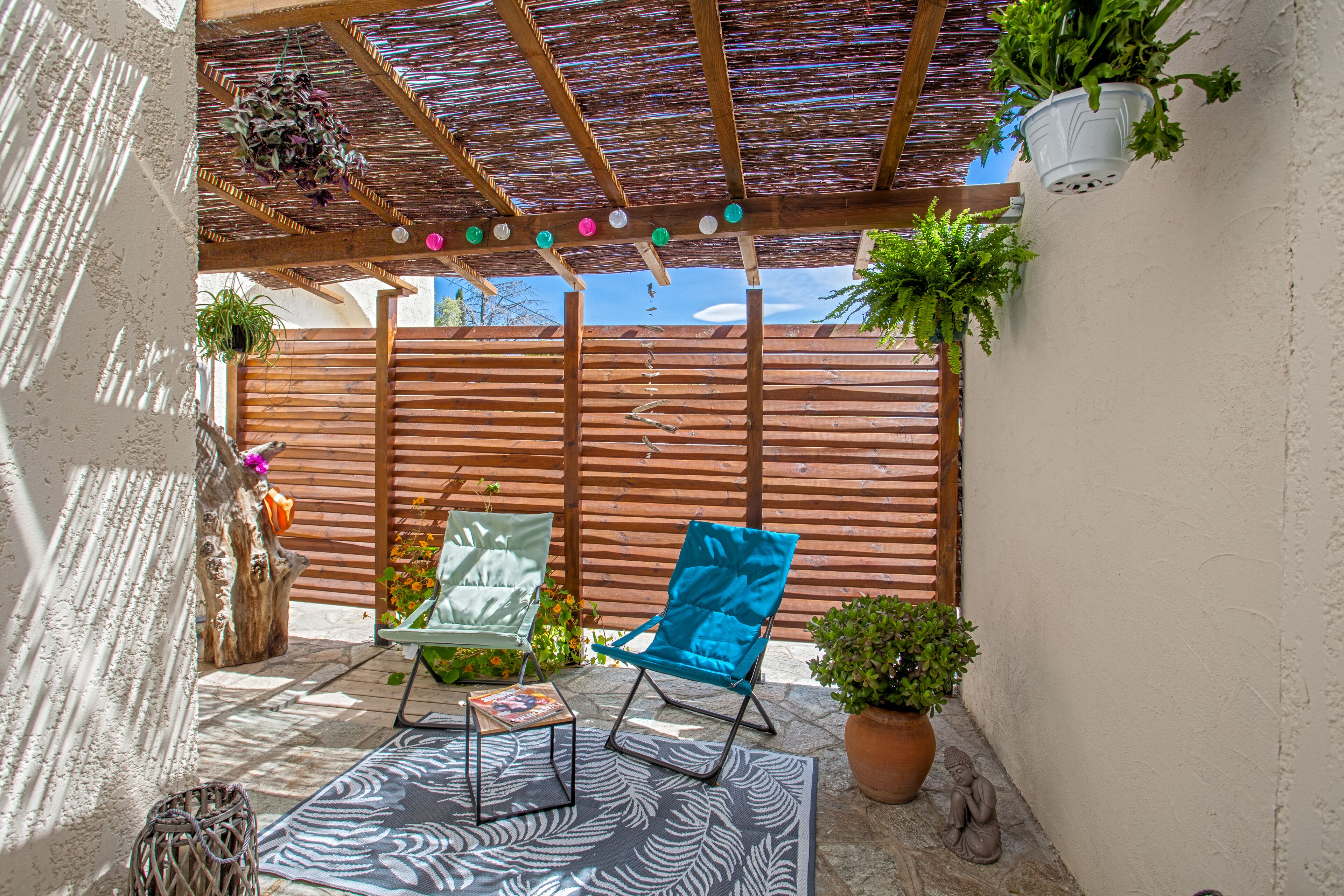 Un espacio de patio cubierto con mobiliario de madera, plantas en macetas y un techo decorativo.