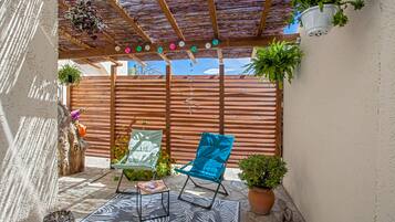Un espacio de patio cubierto con mobiliario de madera, plantas en macetas y un techo decorativo.