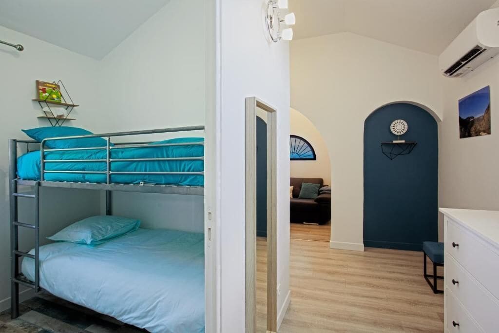 A room with bunk beds, a desk, a chair, a dresser, and a door leading to another room.