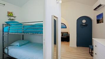 A room with bunk beds, a desk, a chair, a dresser, and a door leading to another room.
