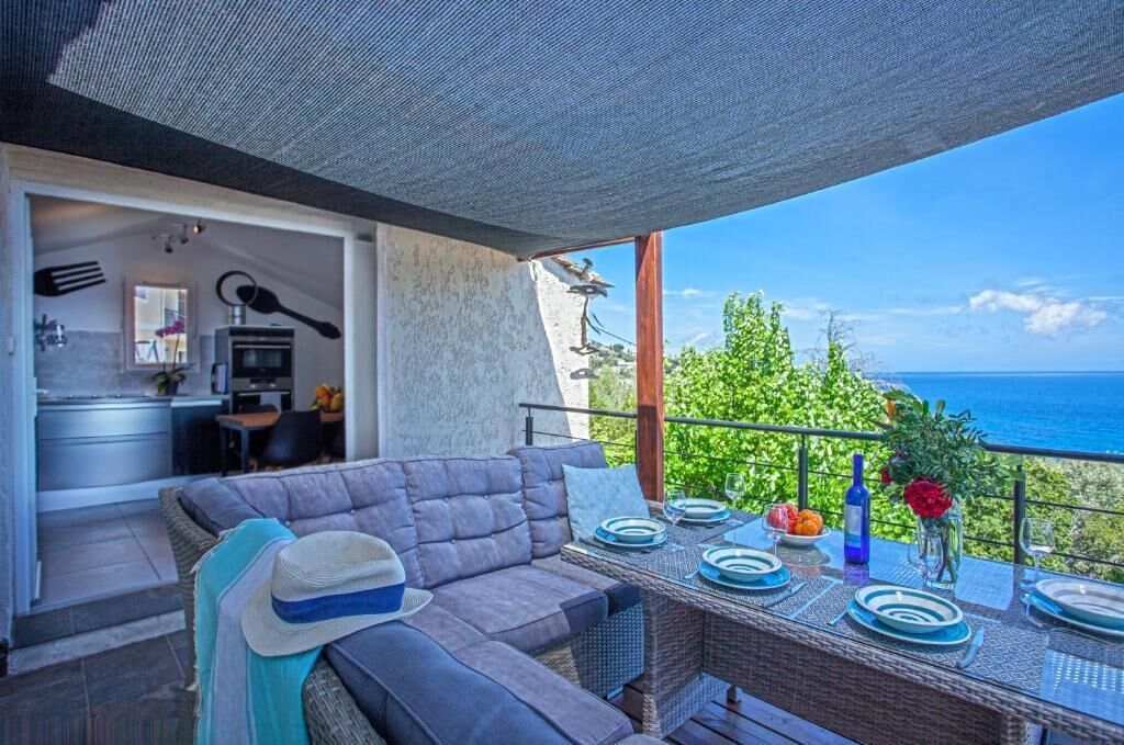 Ein Balkon mit Esstisch für zwei Personen, einer Couch und Blick auf das Meer.