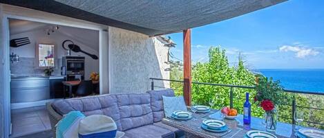 Ein Balkon mit Esstisch für zwei Personen, einer Couch und Blick auf das Meer.