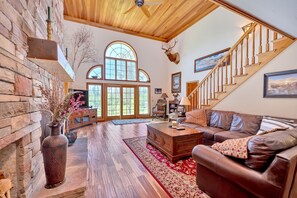 A spacious living room with a large wooden staircase, a fireplace, and a deer head mounted on the wall. - Awesome, 5 bedroom, private Boyne Falls home close to Boyne Mountain. (Boyne Falls)