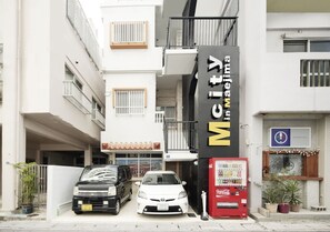 A building with a sign for "Mcity inwebima" and a Coca-Cola vending machine.