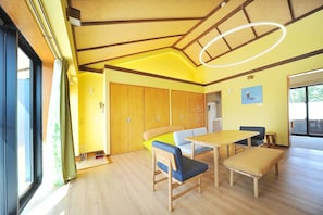 Une pièce avec un plancher en bois, une table à manger avec des chaises, un banc et une grande fenêtre avec des rideaux.