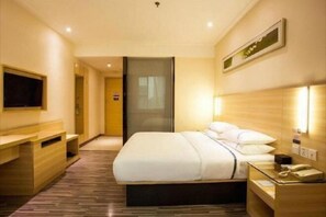 Habitació d'hotel amb llit, taulella de nit, televisió i llum penjada a la paret.