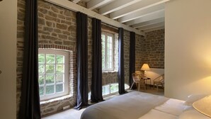 A bedroom with a large bed, stone walls, a wooden floor, and a window with curtains. - La Grange d'Eugénie - Chez Marcelle and Eugénie (Saint-Léger-sur-Dheune)