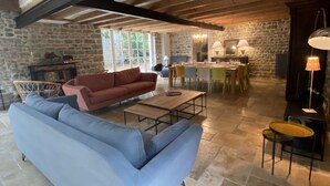 A spacious living area with a stone wall, a wooden ceiling, a sofa, a dining table, and chairs. - La Grange d'Eugénie - Chez Marcelle and Eugénie (Saint-Léger-sur-Dheune)