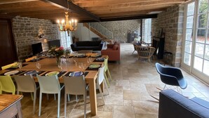 A spacious dining area with a long wooden table set for six, surrounded by chairs. A stone wall and a staircase are visible in the background. - La Grange d'Eugénie - Chez Marcelle and Eugénie (Saint-Léger-sur-Dheune)
