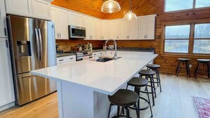 Una cocina moderna con una isla grande, electrodomésticos de acero inoxidable, armarios blancos e iluminación colgante.