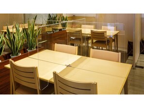 Een moderne eetruimte met glazen scheidingswanden, houten tafels en stoelen.