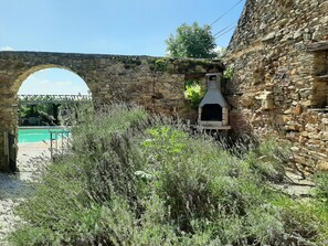 A stone archway, a stone wall with a chimney, and a pool in the background.