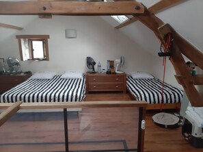 A bedroom with two beds, a wooden ceiling, a small window, and a fan on the dresser.